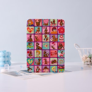 Può includere: Una custodia rettangolare per tablet con un motivo a griglia colorato dei personaggi di Scooby-Doo, tra cui Scooby-Doo, Shaggy, Daphne, Velma e Fred, intervallati da cuori, cupcake, fiori e il furgone Mystery Machine su uno sfondo viola.