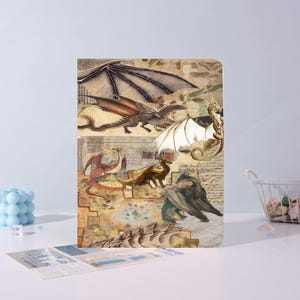 May include: A rectangular journal featuring a collage of vintage-style dragon illustrations. The dragons are depicted in various colors, including brown, gray, and red, set against a backdrop of aged paper and maps. The journal has a soft, matte finish.