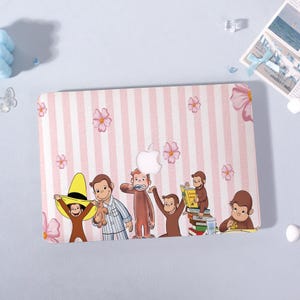 May include: A pink and white striped laptop case featuring a cartoon illustration of Curious George and the Man with the Yellow Hat. The case has a floral pattern and the Apple logo.