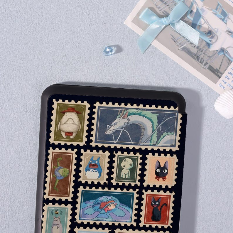 Puede incluir: Una funda de tel&eacute;fono negra con un collage de coloridos dise&ntilde;os de sellos postales. Los sellos representan varios personajes animados, incluyendo un drag&oacute;n blanco, una criatura azul y un gato negro. La funda est&aacute; sobre un fondo azul claro.