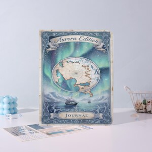 Peut inclure: Un journal intitulé "Aurora Edition" avec un design vintage. La couverture présente un globe, un navire naviguant sur la mer et les aurores boréales en arrière-plan. Le journal est de couleur bleu clair.