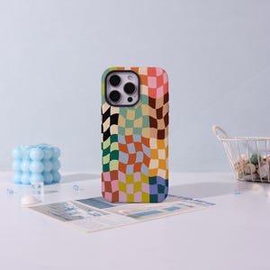 May include: A colorful phone case with a wavy checkerboard pattern in shades of orange, pink, green, yellow, and blue. The case is designed to fit a smartphone and has cutouts for the camera and buttons. The case is on a white surface.