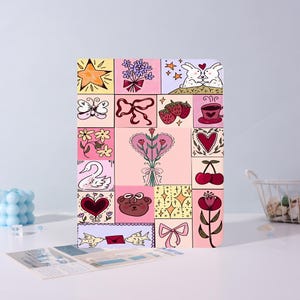 May include: A rectangular notebook featuring a grid of colorful illustrations including a star, a bouquet of flowers, two rabbits, a butterfly, a ribbon, strawberries, a coffee cup, a swan, a heart, a teddy bear, cherries, and a flower.