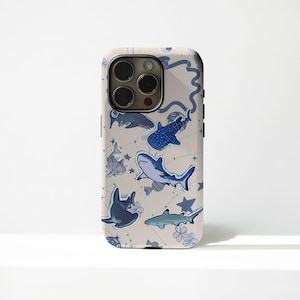 May include: A phone case featuring a pattern of various blue sharks, stars, and floral accents on a light beige background. The case has a glossy finish and a camera cutout.