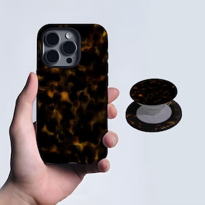 May include: A phone case and matching phone grip featuring a tortoiseshell pattern in shades of brown and gold. The phone case is shown held in a hand, while the grip is displayed separately.