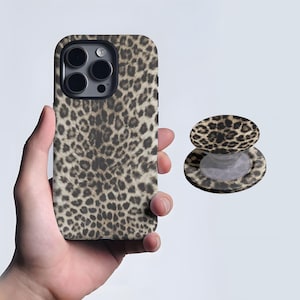 May include: A leopard print phone case and matching phone grip. The case is on a phone and the grip is separate. The print is a mix of black and brown spots on a tan background. The phone case has a black camera lens.