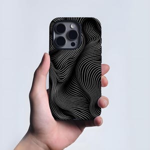 May include: Black and white phone case featuring a flowing, striped design. The case has a minimalist aesthetic. The phone case is held in a hand.