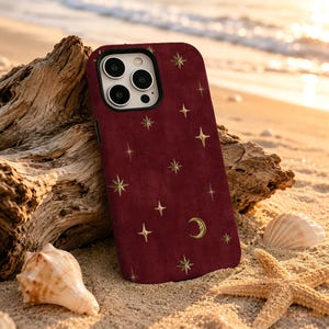 May include: A deep red smartphone case featuring a repeating pattern of gold-colored four-pointed stars and a small crescent moon. The case has a rectangular cutout for the camera lenses and is designed to fit a modern mobile device.
