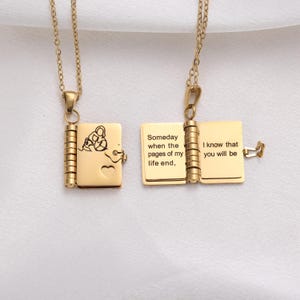 May include: Two gold-colored, open book pendant necklaces. One pendant has a lock and key design with a heart. The other pendant has the text: "Someday when the pages of my life end, I know that you will be."