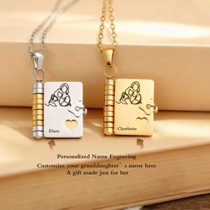 Puede incluir: Dos collares con colgante, uno plateado y otro dorado, cada uno con un pequeño medallón con forma de libro. Los medallones tienen un recorte en forma de corazón y un dibujo de una persona con un niño. El medallón plateado dice "Elara", y el dorado "Charlotte".