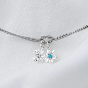 May include: A silver chain necklace with a knot design and two flower charms. One charm is a silver flower with a clear crystal center, and the other is a silver flower with a blue crystal center.