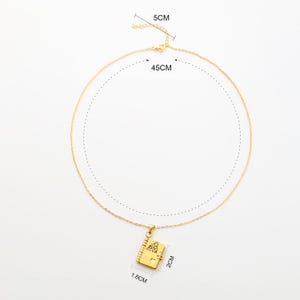 May include: Gold-colored necklace with a pendant shaped like a small book. The chain is 45 cm long, and the pendant is 1.6 cm wide and 2 cm high. The clasp is 5 cm long. The book pendant has a detailed design.