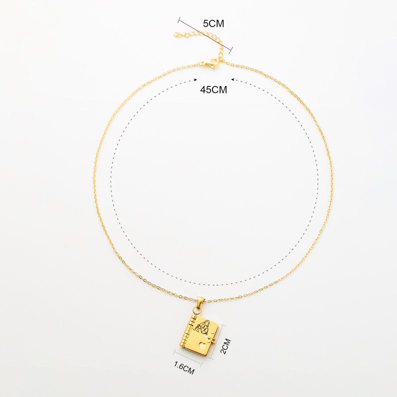 May include: Gold-colored necklace with a pendant shaped like a small book. The chain is 45 cm long, and the pendant is 1.6 cm wide and 2 cm high. The clasp is 5 cm long. The book pendant has a detailed design.