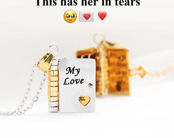 Puede incluir: Un collar con un colgante de libro plateado y dorado con las palabras "My Love" y un detalle en forma de corazón. El texto "This has her in tears" está encima del colgante.
