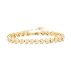 Op de afbeelding: Een goudkleurige armband met hartvormige schakels, elk met een kleine, heldere edelsteen. De armband heeft een verstelbare ketting. De sieraden worden gepresenteerd tegen een witte achtergrond.