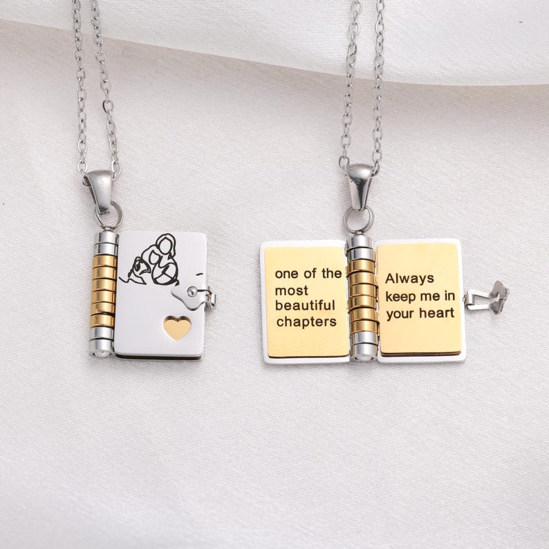 May include: Two silver necklaces with book-shaped pendants. One pendant is closed, with a family silhouette and heart cutout. The other pendant is open, with the words "one of the most beautiful chapters" and "Always keep me in your heart".