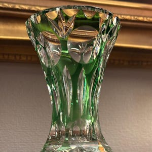 May include: A green glass vase with detailed cut patterns. The vase features a flared top and a rounded base. The cut glass design creates a play of light and shadow, enhancing its decorative appeal. The vase is likely used for displaying flowers.