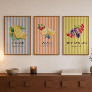 Peut inclure: Trois cadres muraux présentant des illustrations à l'aquarelle de fruits sur des fonds rayés. Le premier montre des citrons avec le texte LIMONE Cucina & Sole, le deuxième un ananas avec ANANAS Cucina & Sole, et le troisième des baies avec FRUTTI di BOSCO Cucina & Sole.