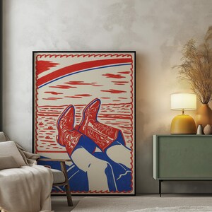 May include: A framed art print featuring a stylized illustration of red cowboy boots with intricate designs, set against a blue and white background. The artwork has a red border and a red and blue arch at the top.