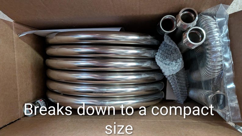 May include: A collection of shiny, silver metal coils and fittings, neatly arranged inside a cardboard box. The text "Breaks down to a compact size" is visible. The components appear to be plumbing or industrial parts.