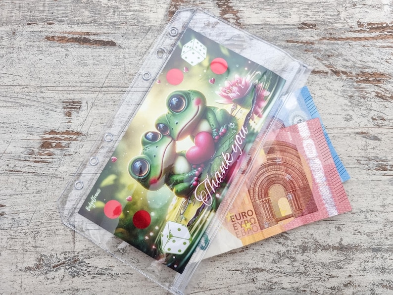 May include: A clear plastic binder pouch with a colorful illustration of two cartoon frogs embracing, holding a heart, with the words "Thank you". Euro banknotes are visible inside the pouch.