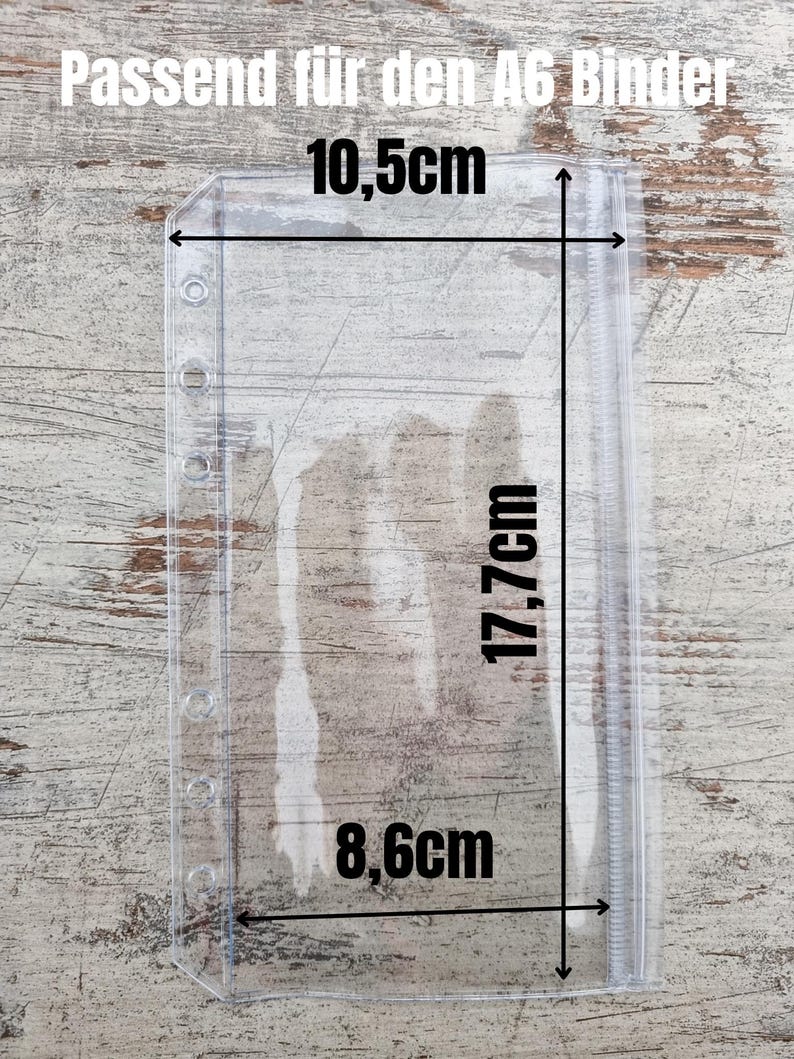 May include: Clear plastic A6 binder pocket with measurements: 10.5cm wide, 17.7cm tall, and 8.6cm wide. The text "Passend f&uuml;r den A6 Binder" is at the top. The pocket has holes for binding and a zipper closure.