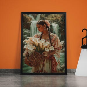 Könnte beinhalten: Gerahmter Kunstdruck mit einer Frau, die einen Korb mit weißen Calla-Lilien hält. Das Kunstwerk zeigt eine Frau in traditioneller Kleidung vor einem Wasserfall. Der Druck ist in einem schwarzen Rahmen und vor einer orangefarbenen Wand.