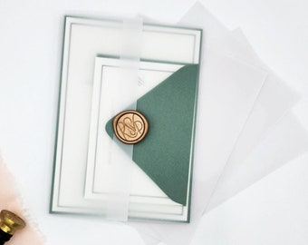 May include: A set of wedding invitations with a green envelope, a white inner envelope, and a clear outer envelope. The envelope is sealed with a gold wax seal. The invitations are tied with a white ribbon.