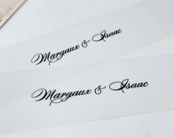 May include: Two white, translucent, rectangular cards with the text "Margaux & Isaac" printed in black cursive script.