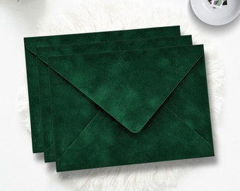 May include: Three emerald green velvet envelopes stacked on top of each other. The envelopes are a deep, rich green color and have a soft, velvety texture.