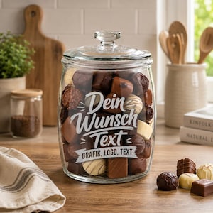 Può includere: Un barattolo di vetro trasparente con coperchio riempito con un assortimento di cioccolatini al latte, fondenti e bianchi. La parte anteriore presenta la scritta bianca "Dein Wunsch Text" sopra un banner con "GRAFIK, LOGO, TEXT".