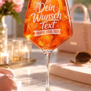 Könnte beinhalten: Ein klares Weinglas gefüllt mit einem orangefarbenen Getränk, Eiswürfeln und einer Orangenscheibe. Das Glas ist mit weißem Text bedruckt, der "Dein Wunsch Text" über einem Banner mit dem Text "GRAFIK, LOGO, TEXT" in fetter Schrift zeigt.