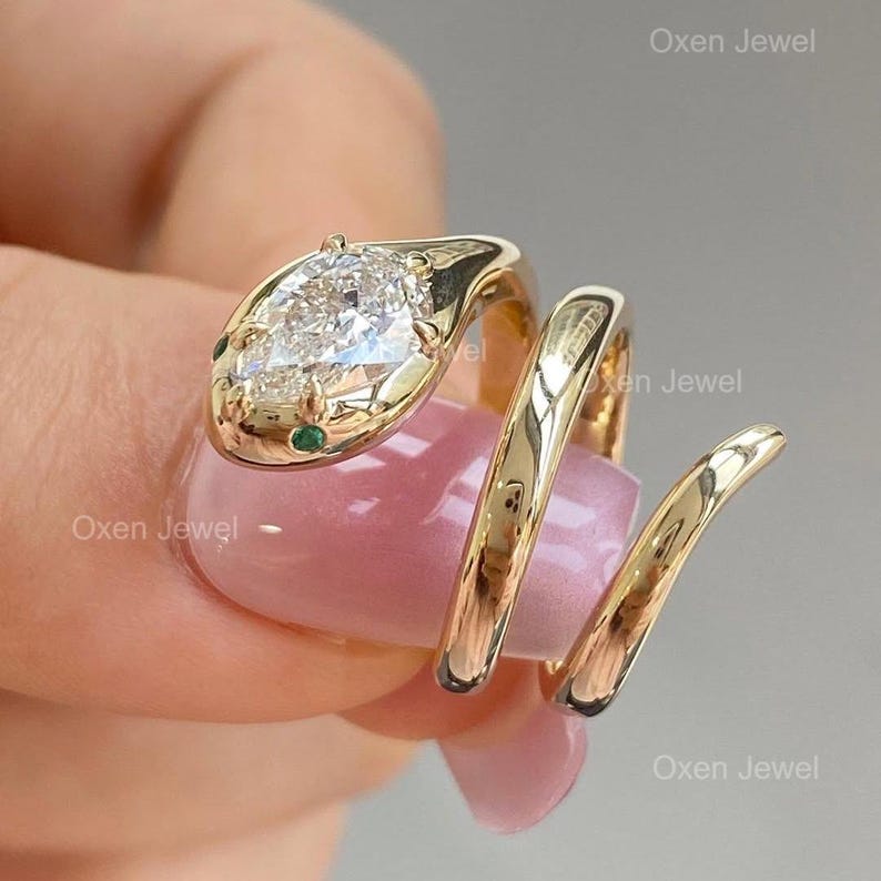 Puede incluir: Un anillo de serpiente dorado con una cabeza de piedra preciosa clara en forma de pera y detalles en verde esmeralda. El anillo se enrolla alrededor del dedo, creando un dise&ntilde;o &uacute;nico y elegante. Es una joya.