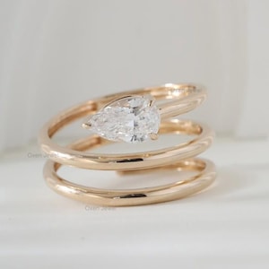 Può includere: Un anello d'oro con un diamante a forma di pera. La fascia dell'anello è progettata a spirale. Il diamante è trasparente e incastonato in una fascia d'oro. L'anello è un gioiello. Il design è elegante e moderno.