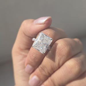 Op de afbeelding: Een ring met een diamant in radiant-slijpvorm met een grote, rechthoekige middensteen. De ring is gezet in een zilveren band en heeft kleinere accentstenen aan de zijkanten. De diamant schittert helder.