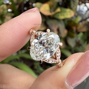 May include: An oval-cut diamond ring set in a rose gold band with small accent diamonds along the setting. The ring features the text OXEN JEWEL printed twice on the metal. The centre stone is a large, faceted oval diamond held by prongs.