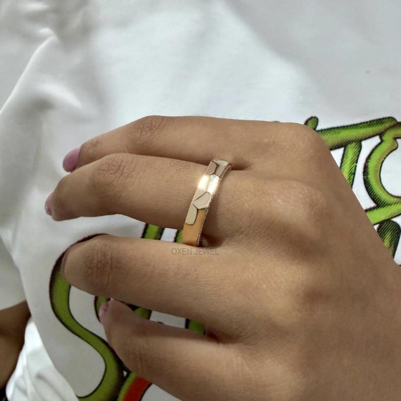 May include: A gold ring with a geometric design. The ring is shown on a hand, with the brand name "OXEN JEWEL" visible. The ring's design features a series of connected, rectangular shapes. The ring is a warm gold color.