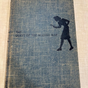 May include: A vintage book titled "The Quest of the Missing Map" with a blue cover. The cover features a silhouette of a person holding a magnifying glass, suggesting a mystery theme. The book's cover has a textured appearance.