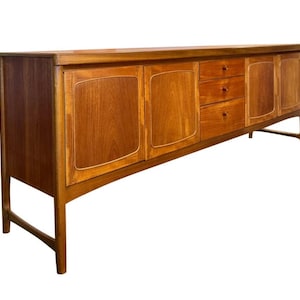 May include: A mid-century modern wooden sideboard with a warm brown finish. It features two sets of doors, three drawers, and angled legs. The doors have a lighter wood trim, and the drawers have round pulls.