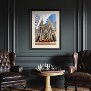 May include: Framed photograph of St. Patrick's Cathedral in New York City, with a yellow taxi cab and other vehicles in front. The image is set in a dark room with two leather armchairs and a chess set on a round table.