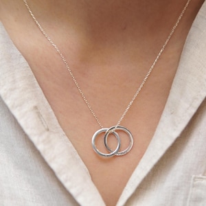 Può includere: Una collana a catena d'argento con due anelli intrecciati. Gli anelli sono incisi con le parole "forever" e "always".