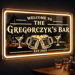 May include: A rectangular LED-lit sign with a black background and warm white glowing border. The text reads "WELCOME TO THE GREGORCZYK'S BAR" and "EST.2025". The design features two clinking beer mugs and two martini glasses with olives.