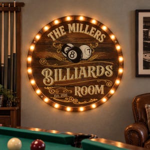 May include: A circular wooden wall sign featuring a dark brown finish and illuminated by a perimeter of warm LED bulbs. The text reads THE MILLERS BILLIARDS ROOM Est. 2026, accompanied by illustrations of an 8-ball and a 7-ball.