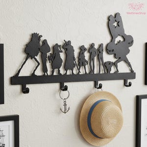 May include: Black metal wall-mounted coat rack featuring silhouette figures and hooks. The rack includes a straw hat with a blue band and an anchor keychain. The text "MethineeShop" is visible.