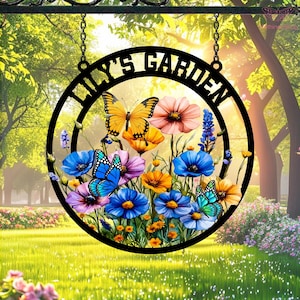 May include: A black metal garden sign with the text "LILY'S GARDEN" in a circular design. The sign features colorful flowers and butterflies. The sign hangs from a chain.