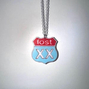 Könnte beinhalten: Halskette mit silberner Kette und Anhänger in Form eines Straßenschildes. Der Anhänger ist oben rot mit dem weißen Wort "lost" und unten hellblau mit den weißen Buchstaben "XX".