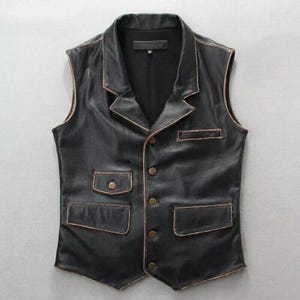 May include: Black leather vest with a notched collar, two front pockets, and four button closure. The vest has a tailored fit and a vintage aesthetic, with subtle brown trim detailing the edges. A classic piece of outerwear.