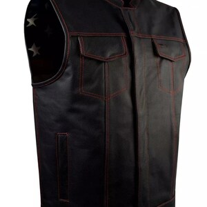 May include: Black leather vest with red stitching and four front pockets. The vest has a stand-up collar and a lining with white stars on a blue background. A classic biker-style vest.