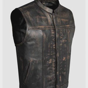 May include: A distressed black leather vest with a stand-up collar and a front zipper. The vest has a weathered appearance with brown accents and a single pocket on the front. The vest is sleeveless and has a classic biker style.