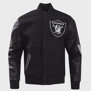 Könnte beinhalten: Schwarze Collegejacke mit weißen Akzenten und dem Raiders-Logo auf der Brust. Die Jacke hat schwarze Lederärmel, einen gerippten Kragen und Bündchen sowie den Schriftzug "Raiders" auf dem Ärmel.